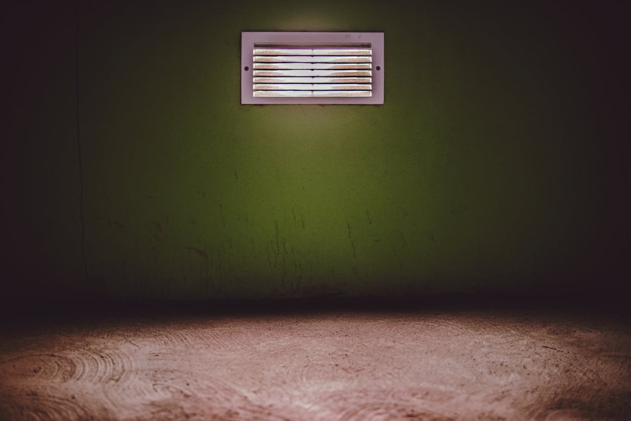 Moody room with a ventilation grate on a textured green wall.