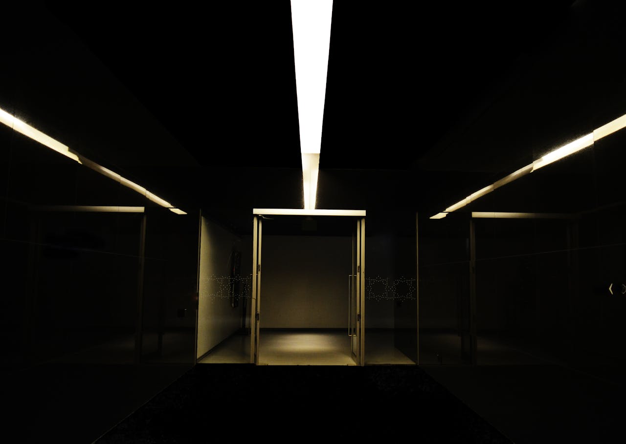 Dark, moody underground hallway with striking linear lighting and steel doors.
