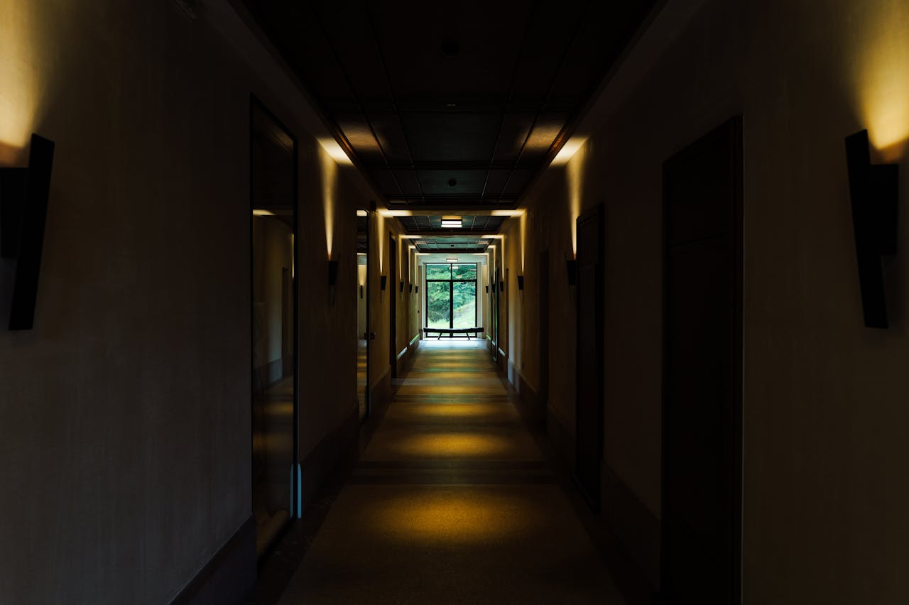 A moody, dimly lit hotel hallway with a window offering a green garden view.